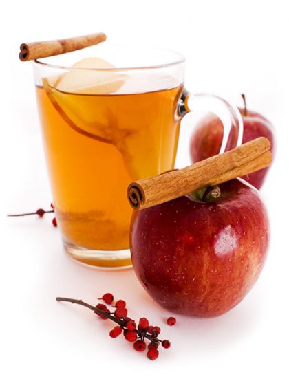 Abbildung des Glüh-Cocktails: Glas-Tasse mit klar-orangener Flüssigkeit. Daneben Äpfel und Zimtrollen.